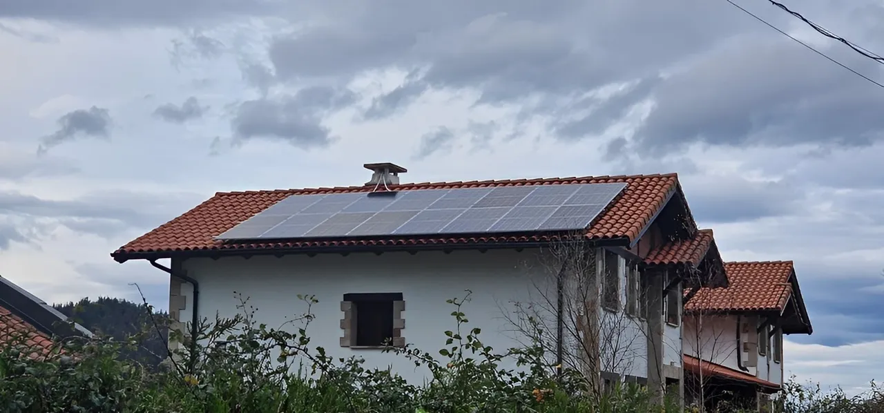 Casa de campo/zona rural con una placa solar en el tejado de tonos rojos.