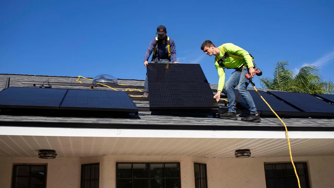 Dos operarios colocan placas solares en un tejado de una vivienda.