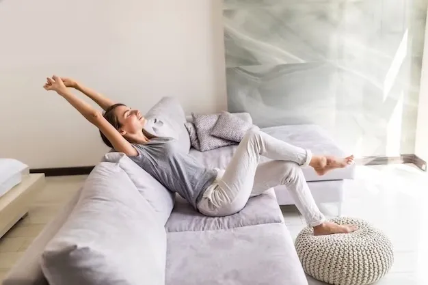 Mujer sentada en su sofá se estira con gesto de relajación.