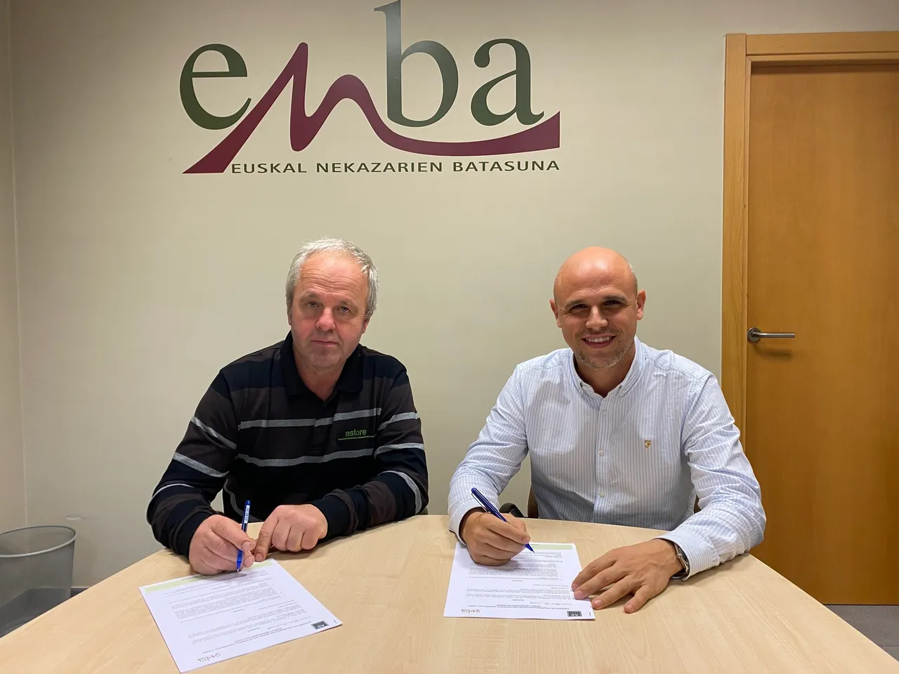 Dos hombres firman un documento en una sala de reuniones.