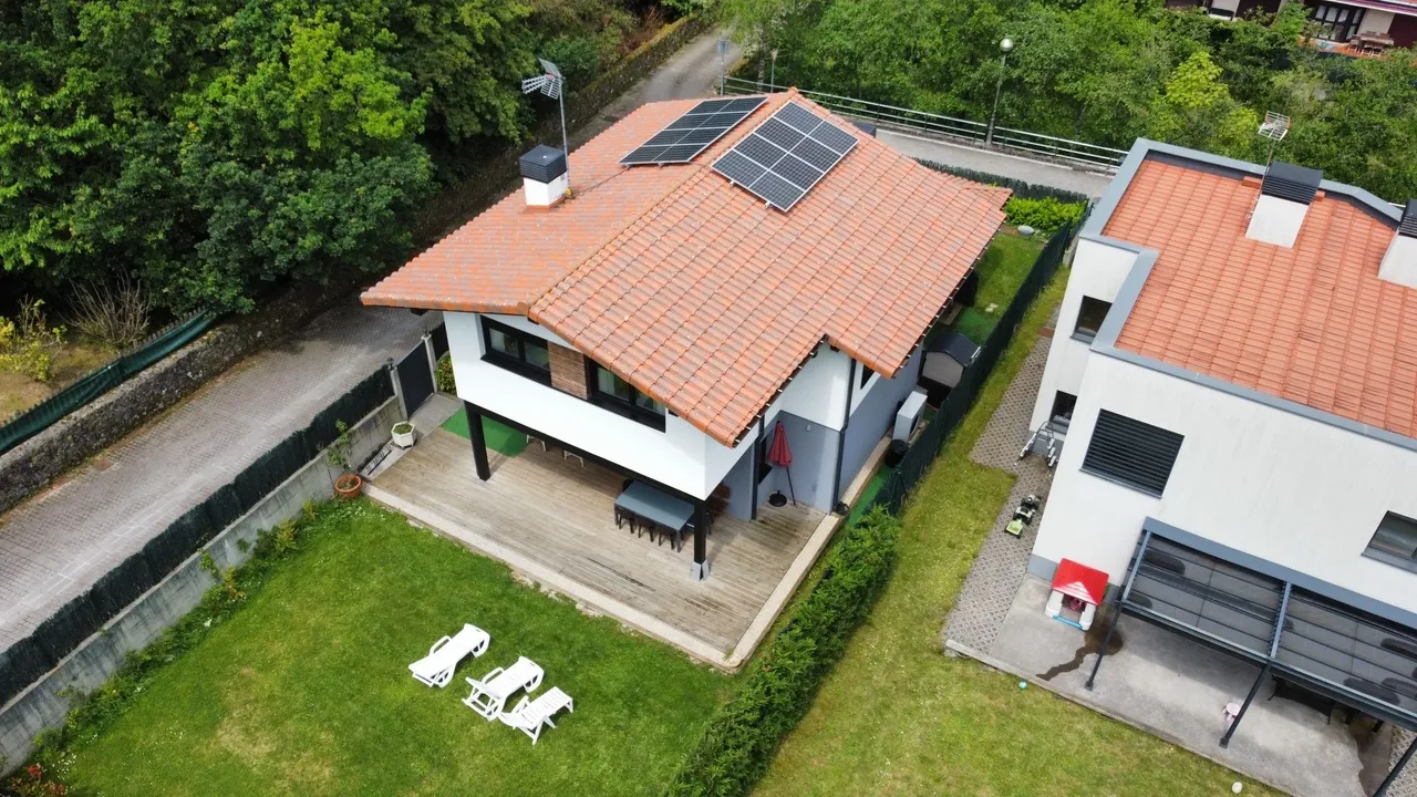 Vista aérea de dos casas con jardín; una de ellas tiene placas solares en el tejado.