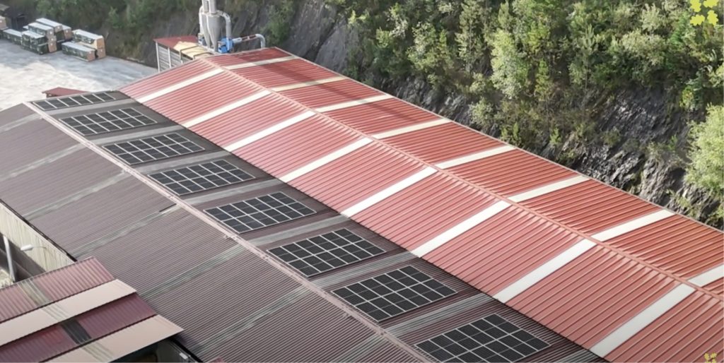 Placas solares en el tejado de chapa de una nave industrial; al lado de esta se encuentra otra nave.